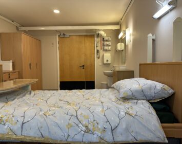 Floral bedspread in single bedroom. Sink and wardrobe in view.